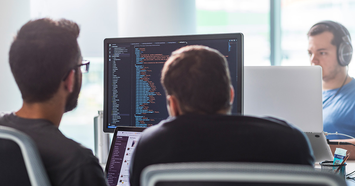 Two men sitting in front of a computer screen displaying code