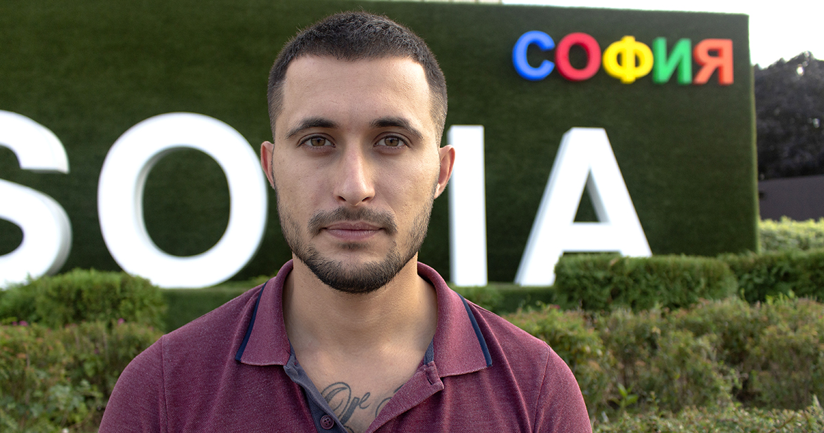 Photo of Daniel with green shrubs behind him and part of sofia sign